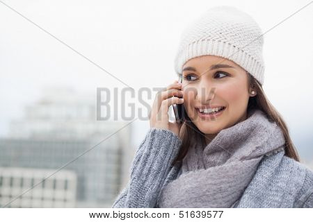 Cheerful brunette with winter clothes on having a call outdoors on a cold grey day
