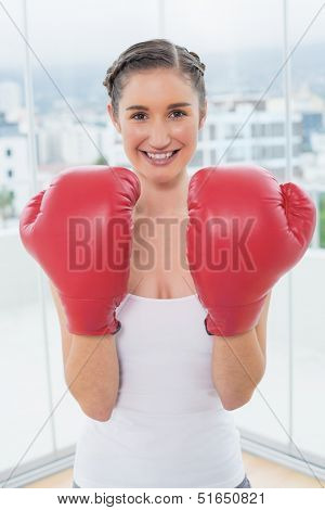 Cheerful sporty brunette wearing boxing gloves in bright fitness studio