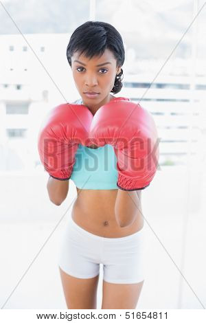 Frowning black haired woman wearing boxing gloves in a living room