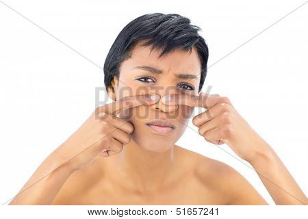 Frowning black haired woman popping a pimple on white background