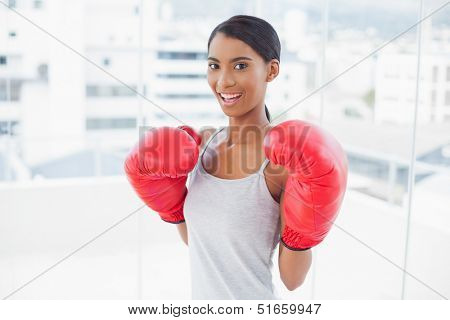 Competitive smiling model wearing red boxing gloves in bright room at home