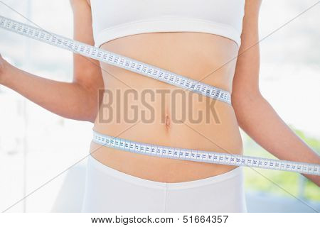 Mid section of woman measuring her waist in bright fitness studio