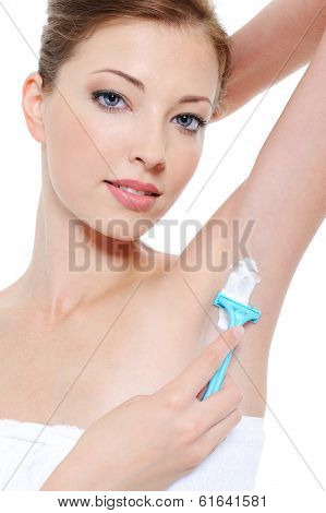 Portrait of pretty young woman shaving underarm with razor