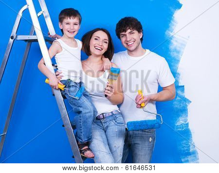 Portrait of happy young family standing together with paintbrush and stepladder