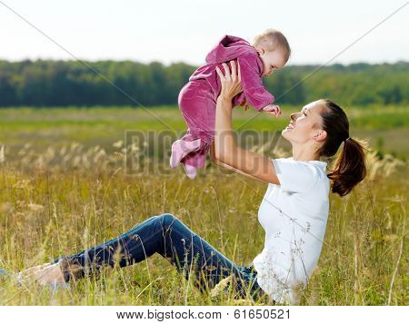 Happy young mather play with smiling baby and throw upwards on nature