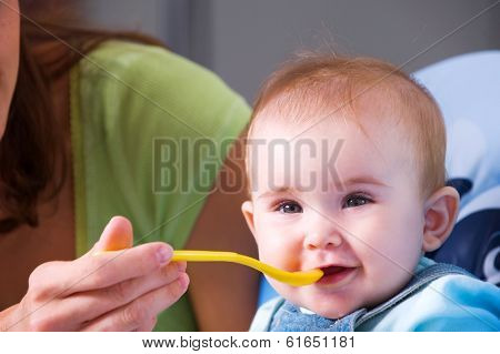 Mother feeding hungry baby in the highchair in kitchen