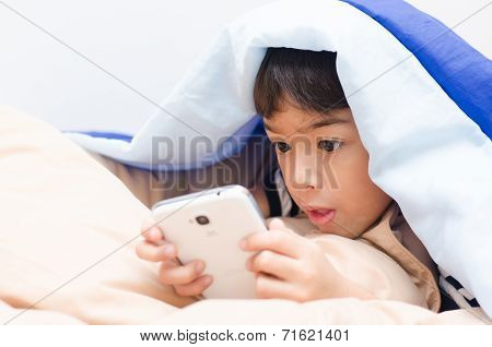 Little Boy Using Mobile Under Blanket