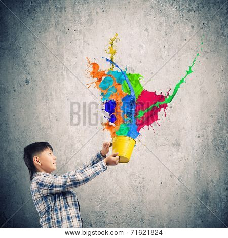 Young boy splashing colorful paint from bucket