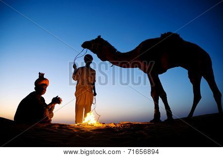 Two indigenous Indian men resting by the bon fire with their camel.