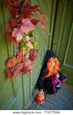Halloween girl in traditional costume sitting on the porch of dilapidated house