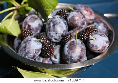 Ripe sweet plums in metal colander, on wooden table