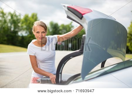 Young, attractive, happy woman taking a suitcase from her car's trunk, smiling, enjoying the travel experience