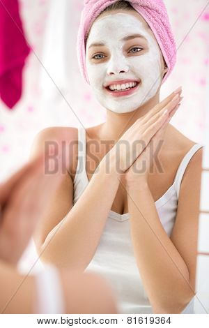 Reflection of happy young girl with  cosmetic facial mask