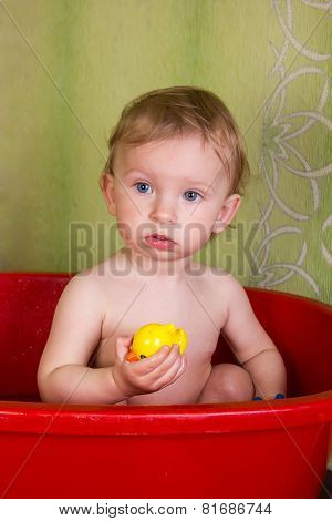 Beautiful little blond girl sitting in the bathroom and chew toys