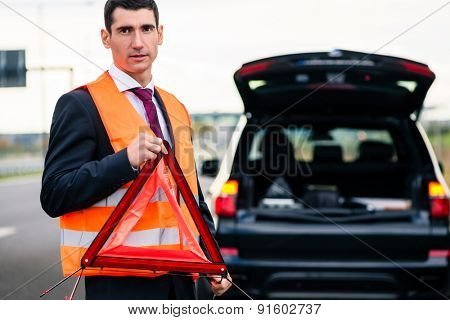 Man with car breakdown erecting warning triangle on road