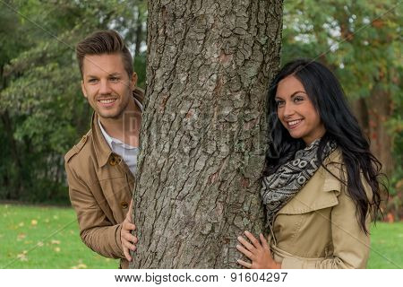 a young, verl liebtes woman looking out from behind a tree