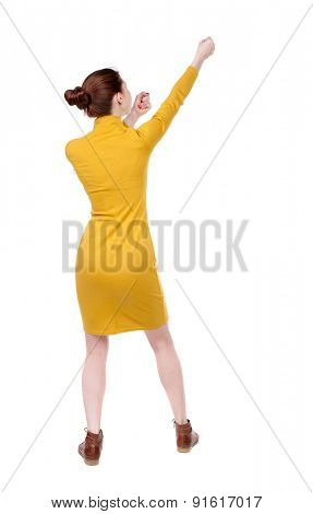 back view of standing girl pulling a rope from the top or cling to something. girl  watching.   Isolated over white background. Girl in mustard strict dress pulling a rope at the top right.