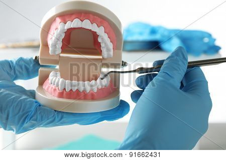 White fake teeth in hand of dentist, on light background