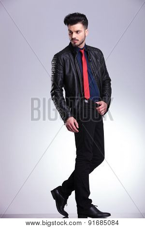 Full body picture of a young casual business man hoding his hand on his belt while looking away from the camera.