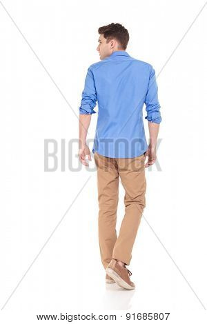 Back view of a young fashion man walking on isolated background looking to his side.