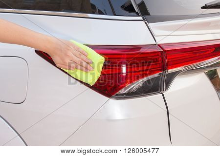 A woman hand with yellow microfiber cloth cleaning big white taillight car.
