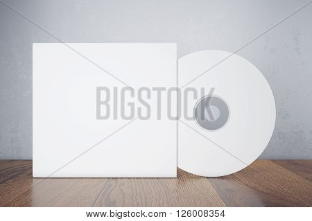 Blank white compact disk with cover on wooden table and concrete wall background. Mock up 3D Rendering