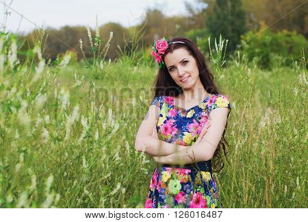 beautiful woman with long hair decorated with artificial flowers stands in a field among the tall grass on a summer evening