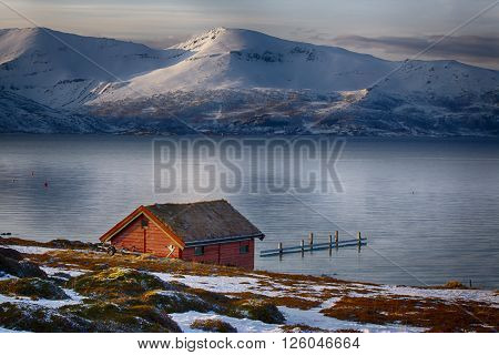 An isolated house on a lake between snowy mountains