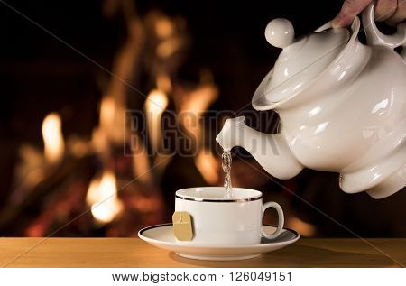 Cup of Tea / Water being poured into a cup of tea with a fireplace on the background