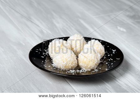 Homemade DIY natural vegan healthy millet gruel and coconut pralines with coconut oil and almond aromate - Rafaello style on a black plate and wooden table. Organic product.