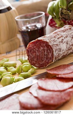 Close up of Italian salami with broad bean over a chopping board and a glass of red wine