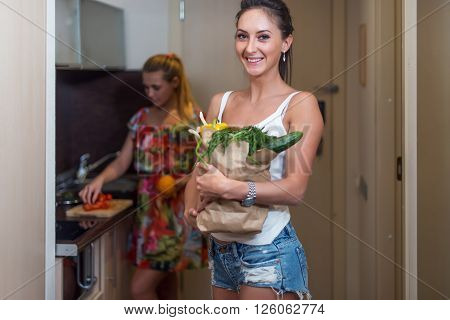 young female roommates in kitchen cooking vegetable salad.