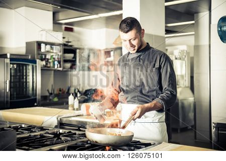 Chef in restaurant kitchen at stove with pan doing flambe on food