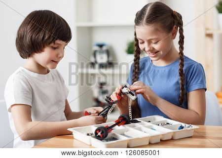 Spent nice time together. Cheerful delighted little children sitting at the table and constructing with lego blocks while    having fun