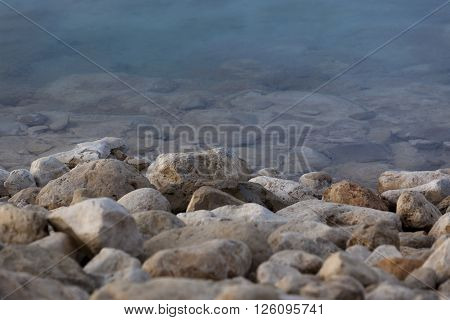 White yellow grey natural boulders with salt levee on blue water edge of Dead Sea