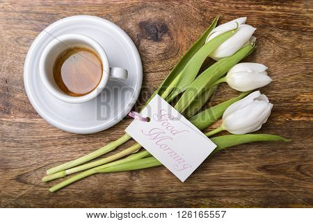 cup of coffee, white tulips and card with good morning written on wooden table top view