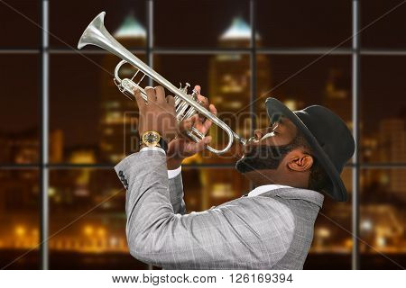 Darkskinned trumpeter in fedora hat. Trumpeter playing in night megalopolis. Music and passion are one. Young talent from capital city.
