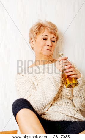 Elderly sad woman sitting in the corner and drinking whiskey
