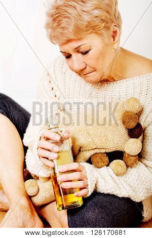 Elderly sad woman sitting in the corner and drinking whiskey