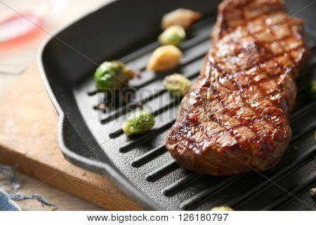Grilled steak with garlic and Brussels sprouts on grill pan, closeup