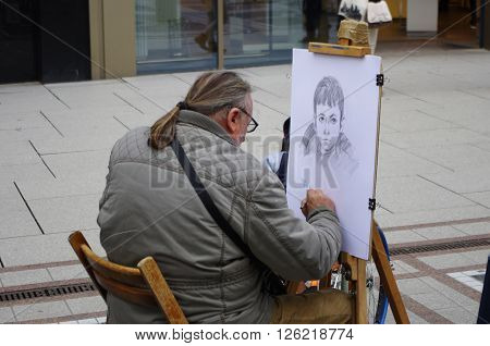 Frankfurt am Main, Hessen, Germany - April 18, 2016: A street artist drawing a picture of a boy. He makes a living by drawing people's face on the street.