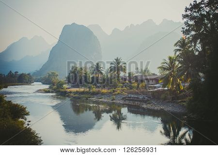 Limestone hills in haze reflected in a river, near Vang Vieng, Laos.