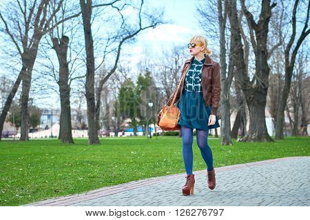 Young woman with leather bag walking in park among the trees