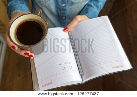 female hands holding a cup of hot coffee and notebook