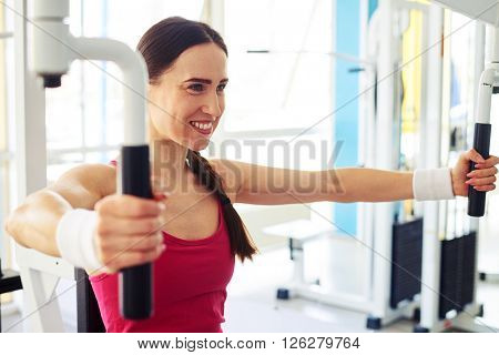 Young beautiful smiling woman is working out on butterfly machine at the gym