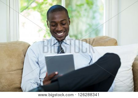 Young man sitting on sofa and using digital tablet at home