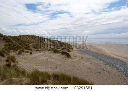 low down shot of beach with pebbles, grassy dunes and contrasting sky in Ynyslas, Wales, UK