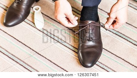 A young man tying elegant shoes indoors.