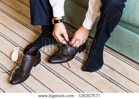 A young man tying elegant shoes indoors.