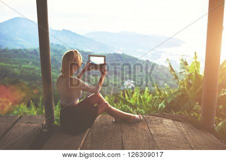 Female traveler is shooting video on portable touch of a wonderful Amazon view during her unforgettable summer weekend. Young woman tourist is taking photo with digital tablet camera of jungle view